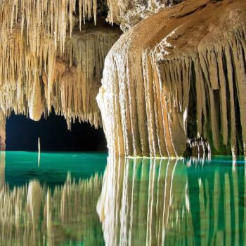 The underground river in Mexico's Yucatan with its white stalactites and stalagmites running into a deep green and blue cenote