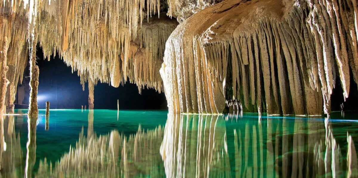 The underground river in Mexicos Yucatan with its white stalactites and stalagmites running into a deep green and blue cenote