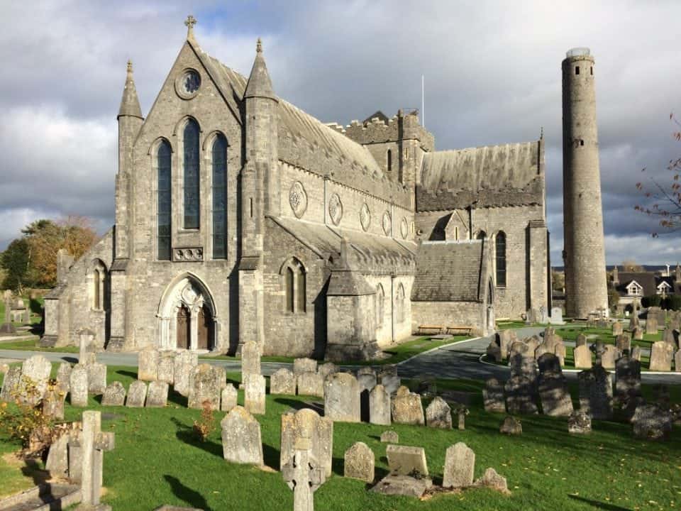 View of St. Canice's Cathedral with gravestones and round tower to the right of the church.