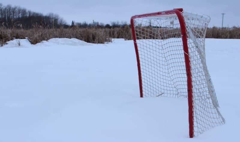 A frozen snow covered scene with trees in the far distance and a single hockey net sitting in the snow.