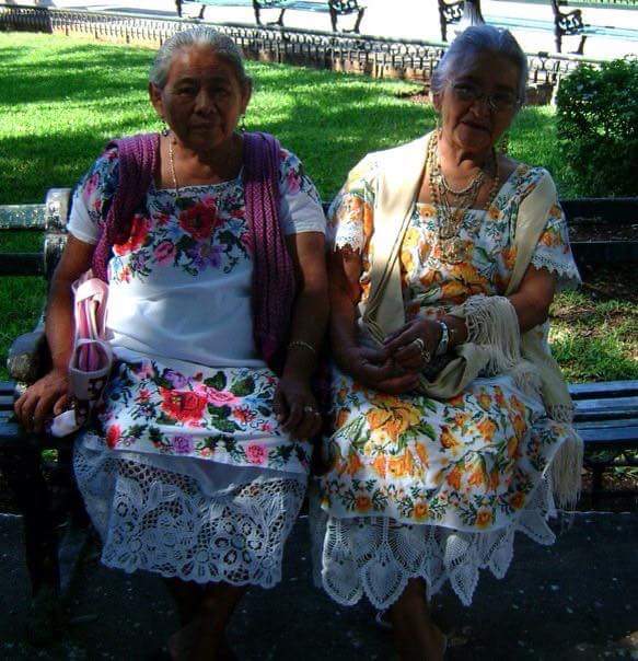 dressed in traditional mexican embroidered dresses at the square. Two elderly ladies are enjoying the sunshine on a park bench