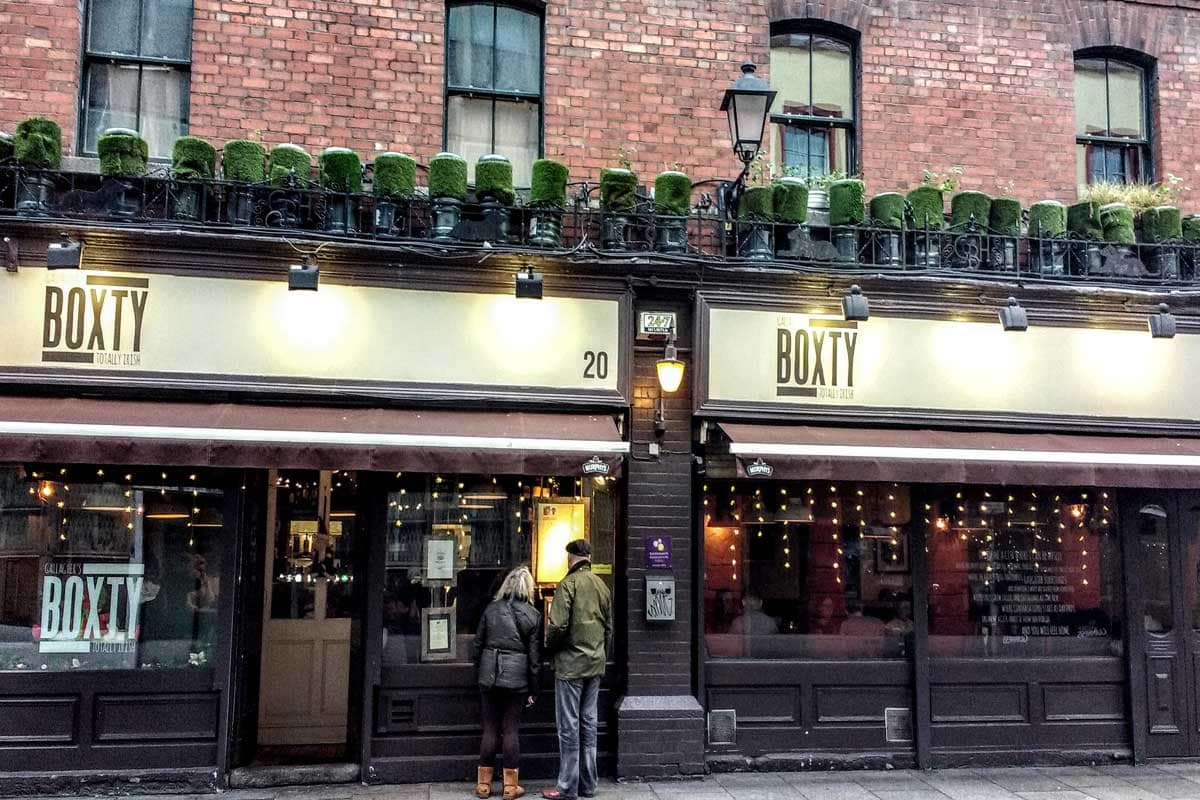 A man and woman are standing outside of an Irish restaurant, contemplating whether to order the traditional boxty - a delicious Irish potato pancake.