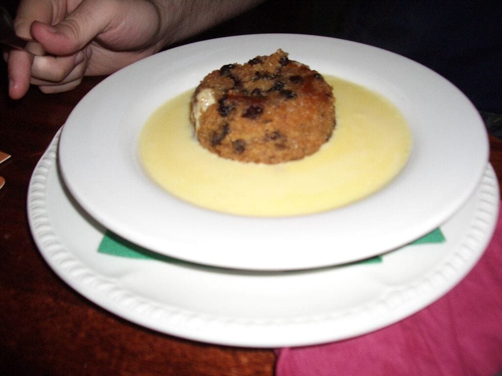 Spotted Dick a British pudding made with suit and lots of raisins then boiled and served in a white bowl with rich custard