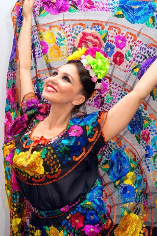 A lady dancing with an embroidered circle skirt the skirt is white with fabulously coloured embroidery and the top is black with lots of coloured flowers embroidered on it