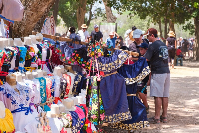 A market day where a woman is selling Mexican embroidered dresses underneath a tree.