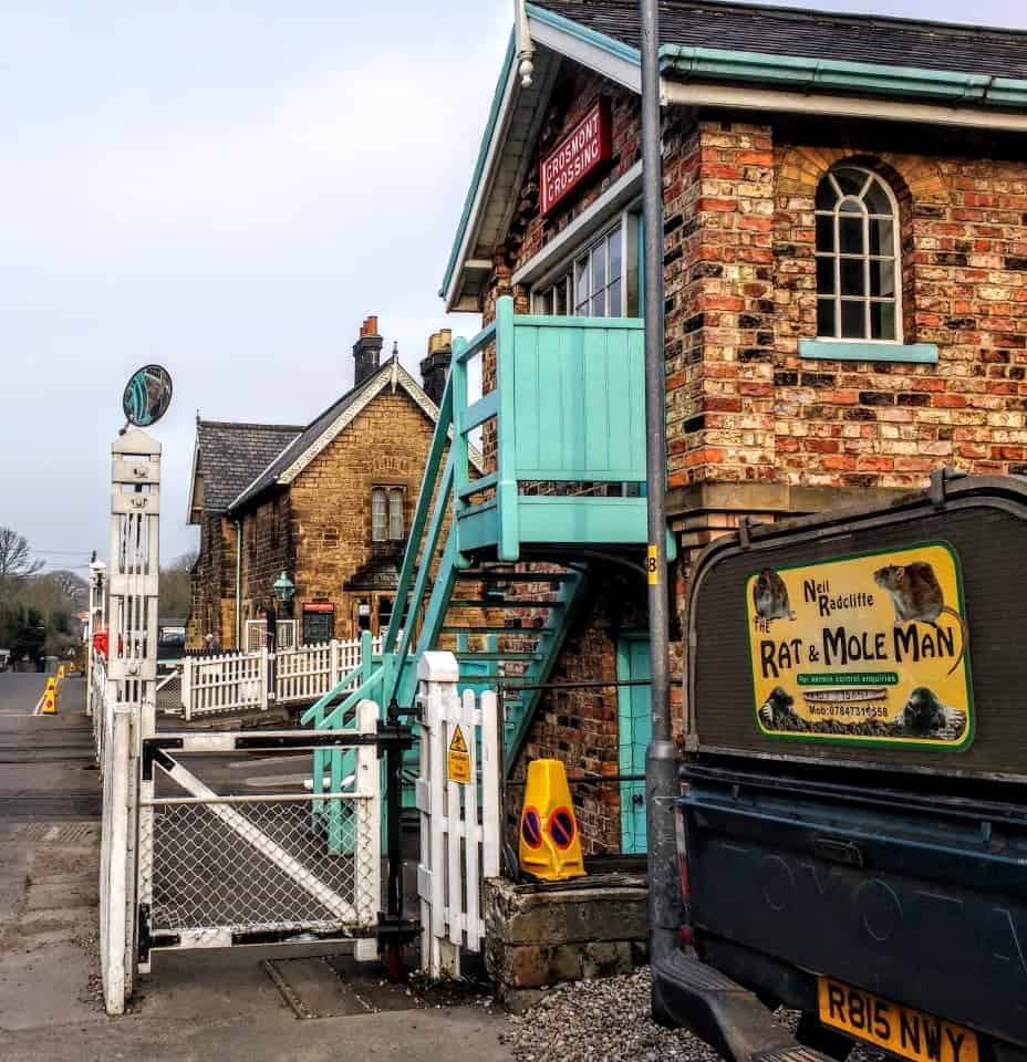 North York Moors Railway Harry Potter train station the signal booth crossing the tracks at Grosmont station with the Rat and Mole Man van sitting outside
