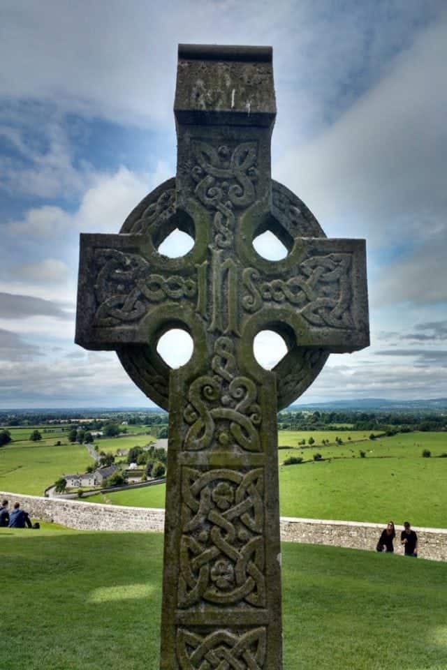 Celtic Cross at the Rock of Cashel. A finely detailed stone cross overlooking the valley of tipperary. The cross has a circle around the centre point of the bar on the cross with intricate celtica knotwork carved on both the cross bar and the stem. 