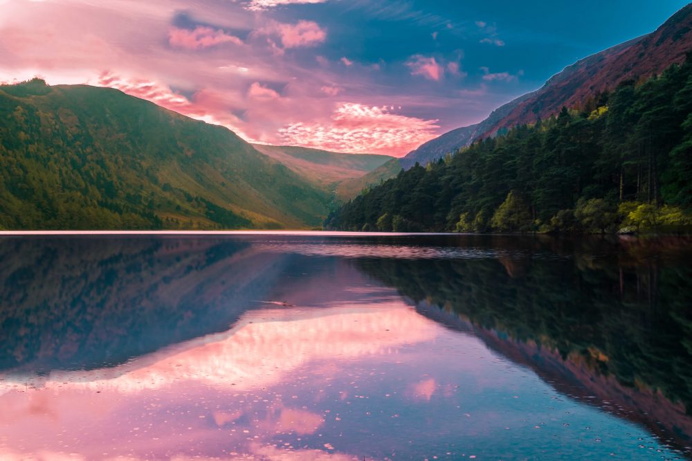 A view of the stunning Wicklow Mountains over the upper lake at sunrise with pink and blue sky and a mirror reflection in the lake
