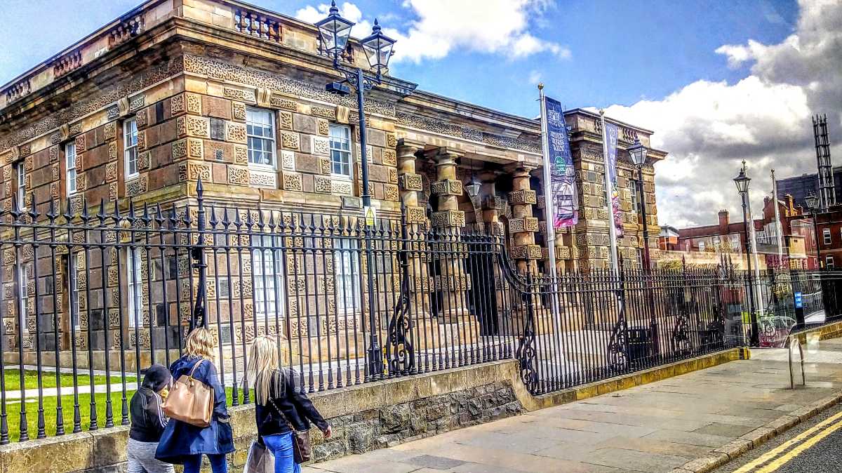 Crumlin Road Gaol from the outside an old run down building with yellow brick and large columns on the front and an iron fence all around the propery