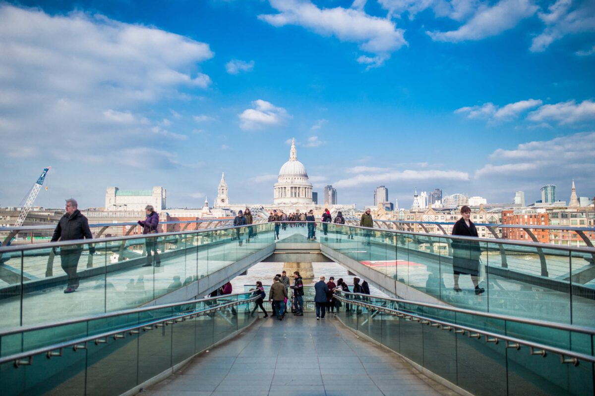 Historical places in the UK a view of St Pauls Cathedral over the pedestrian bridge of the Thames. Blue skies and people walking along the brdige