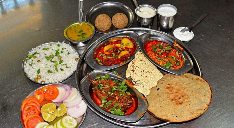  a selection of the national dishes of India platters of white rice pilaf, fresh sliced vegetables and various curries and naan bread.