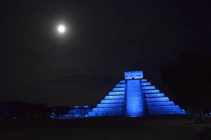 chichen itza at night with a full moon and the building lit up with blue lights