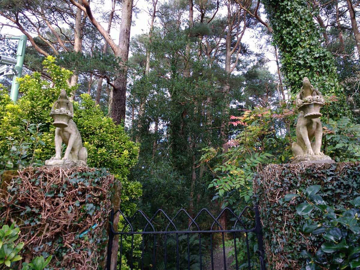 two statues at the gate into Glenveagh Castle Gardens. the dogs are holding bamskets with flowers in the