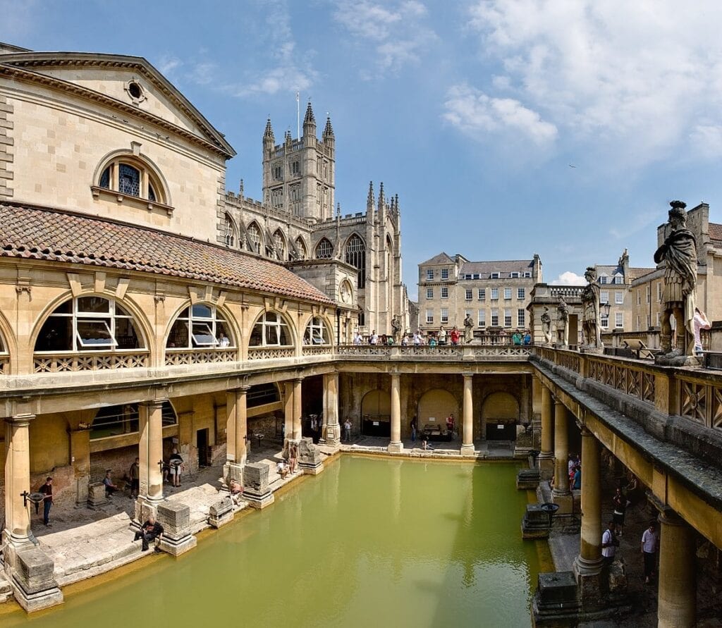City of Bath with the Roman baths. Figures mount the exterior walls and the interio pool is greenand the arches support the exterior walls