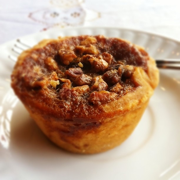A small single serving butter tart with a golden shortcrust pastry shell and the butter and sugar filling with pecans on the top