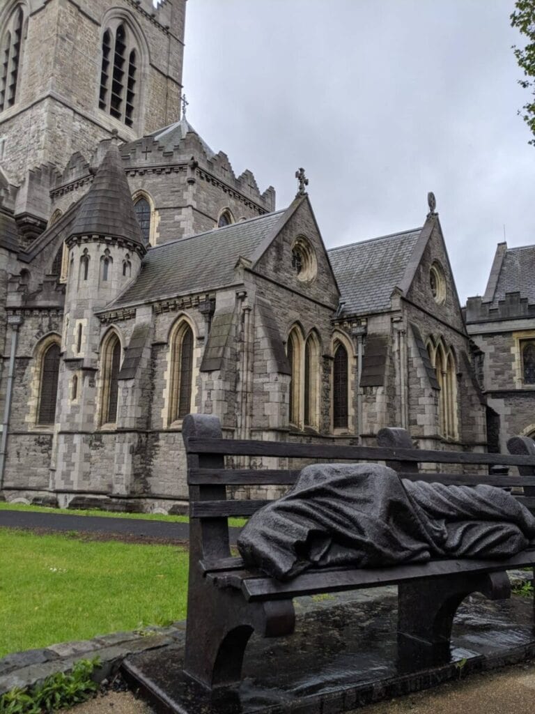 Christchurch Cathedral Dublin the exterior of the cathedral with a statue of a homeless person sleeping on a bench