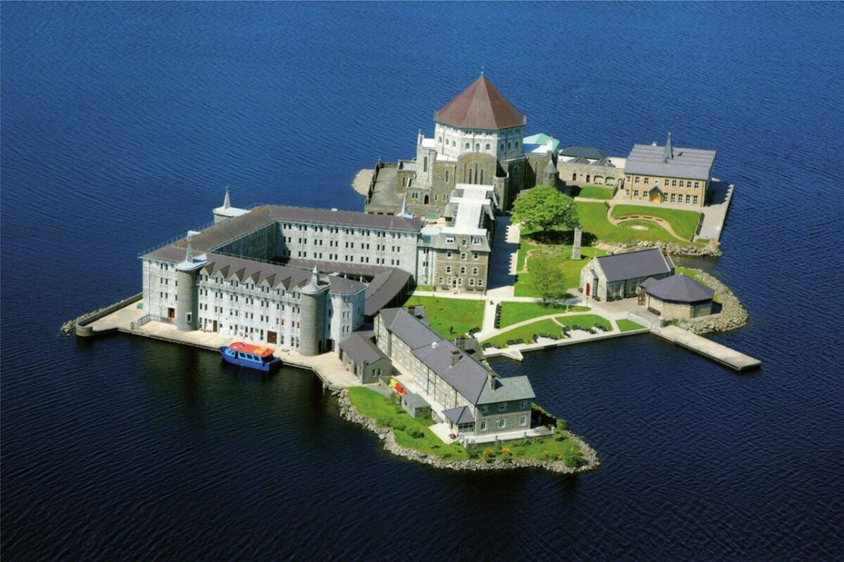 view of Lough Derg from a drone things to do in Donegal. The Sanctuary of the famous Irish saints - Saint Patrick sits in them middle of a beautiful blue lake, the white buildings look like an old castle with turrents and rounded capped roofs. 