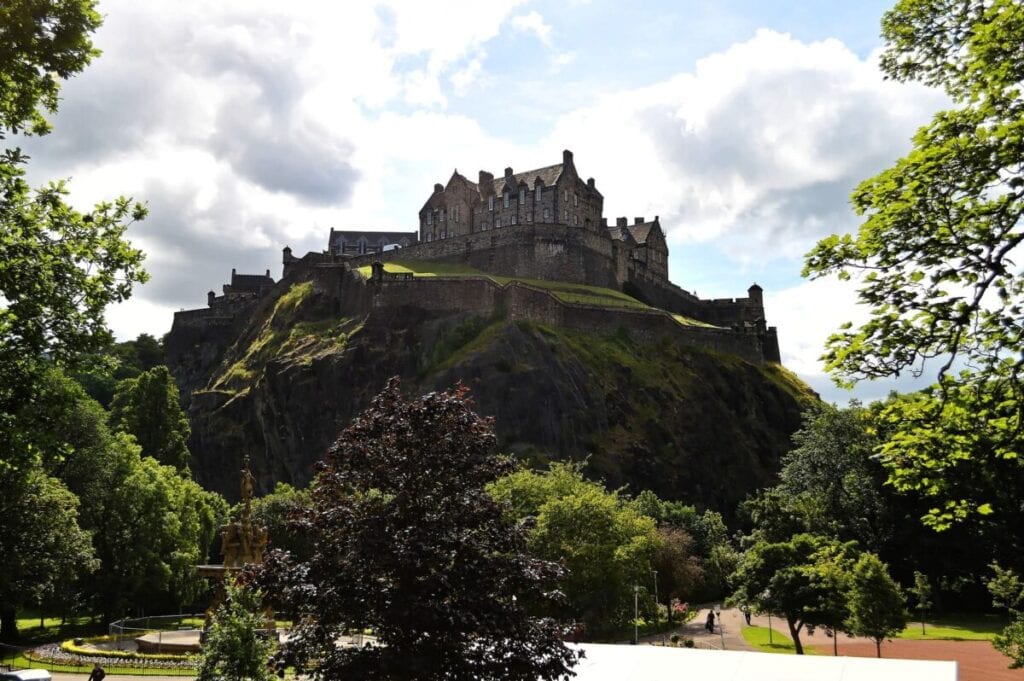 Edinburgh Castles stands proudly on top of a large granite cliff covered in greenery.