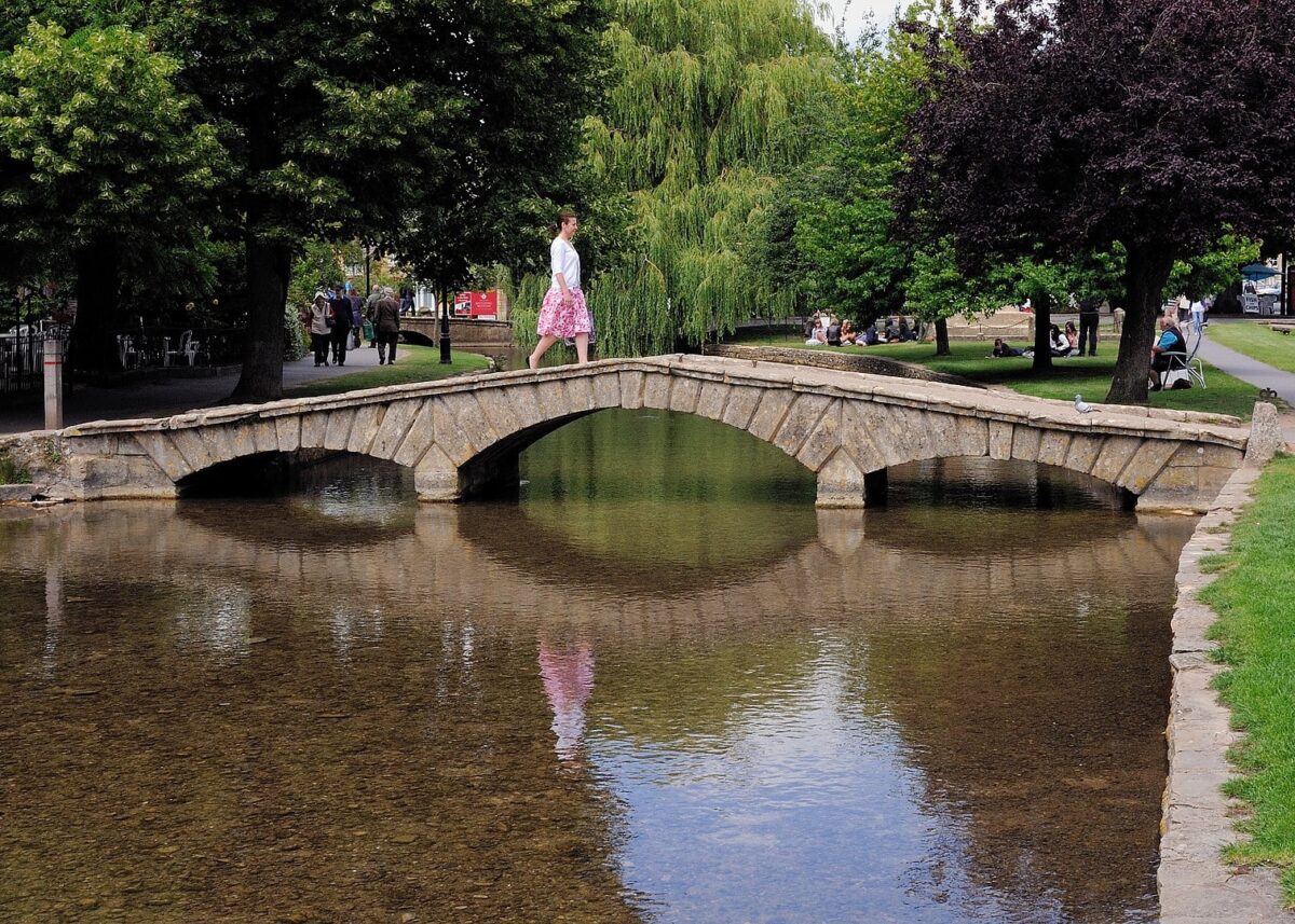 crossing an old stone bridge in one of the prettiest Cotswolds Village.