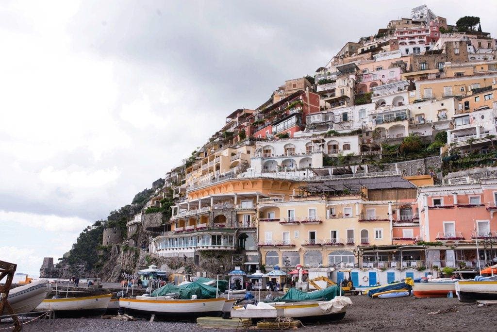 View of the town of Capri rising up along the hillside from the marina which is full of white and gold fishing boats. 
