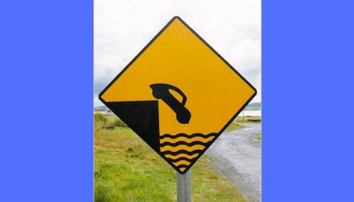 A yellow road sign featuring a car plunging into the water, showcasing an amusing example of Irish Slang.