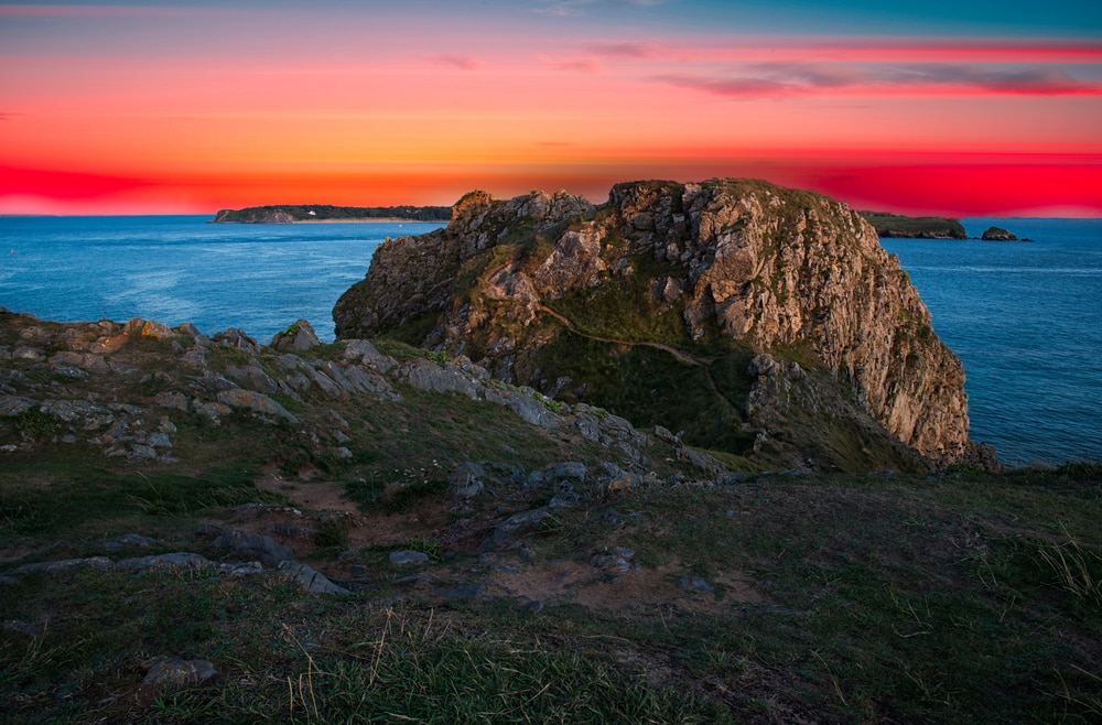 Giltar Point one of the most beautiful beaches in Pembrokeshire at sunset the sky is pink, blue, orange and red streaked and the point is dark in the foreground with a hint of the hills and valleys