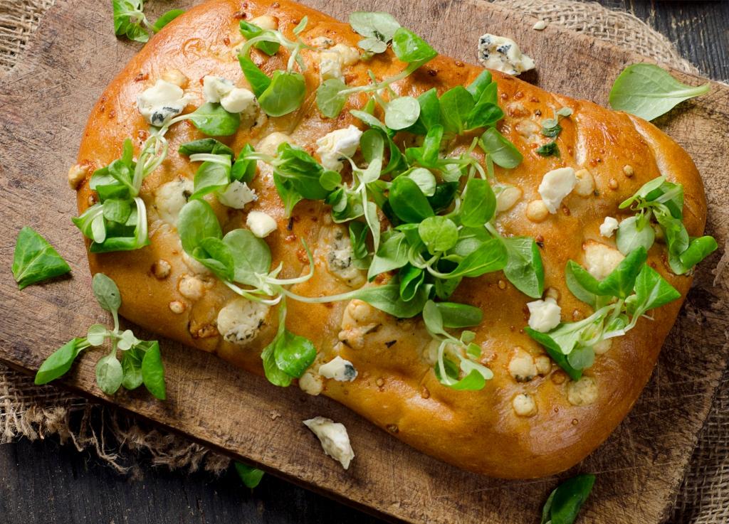 Homemade Italian Focaccia bread sprinkled with green onions, pea shoots and parmesan
