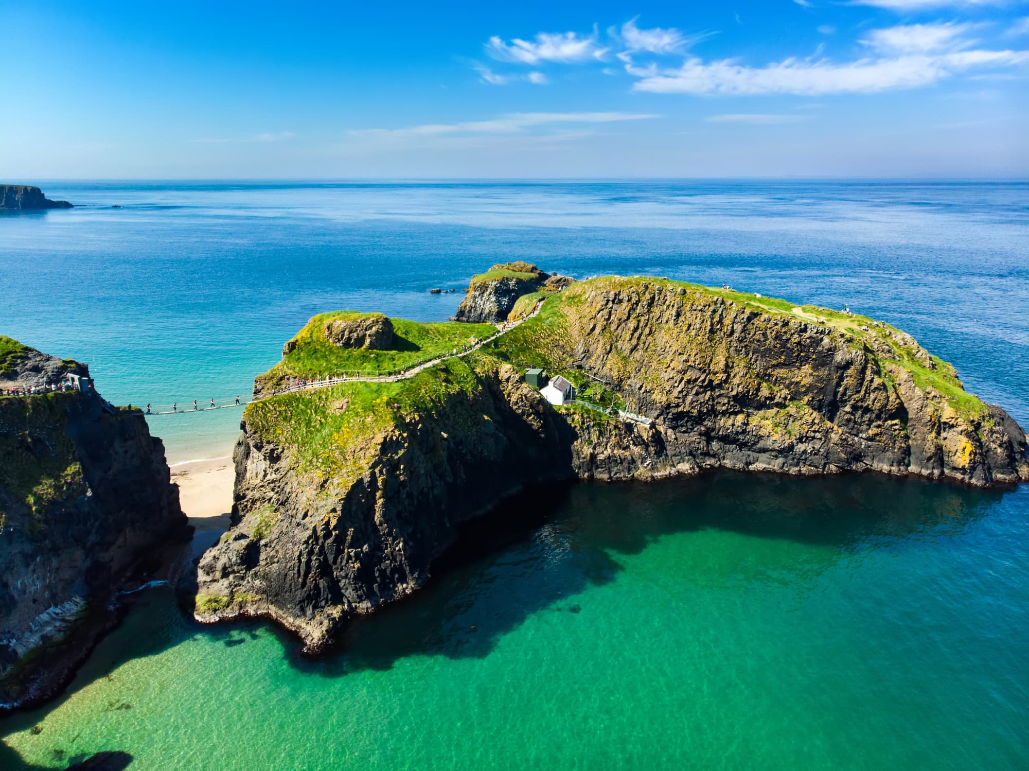 a view of the rope bridge of Carrick-a-rede from the shore. Showing a line of tiny people crossing the rope bridge to the island of Carrick