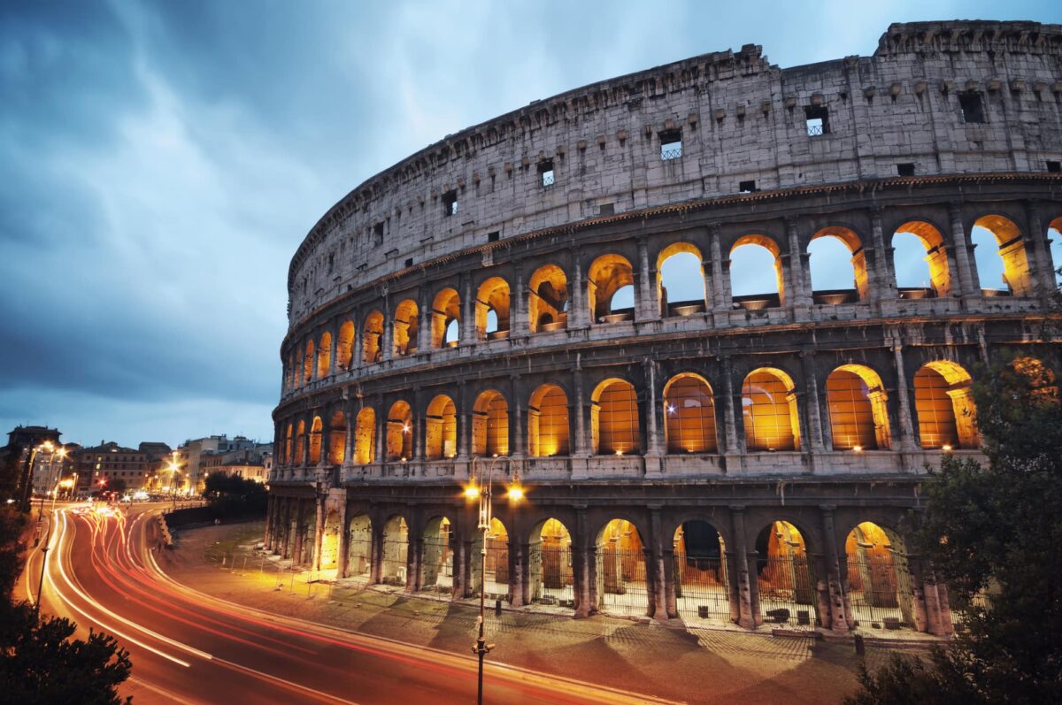 Coliseum at night with colorful blurred traffic lights.