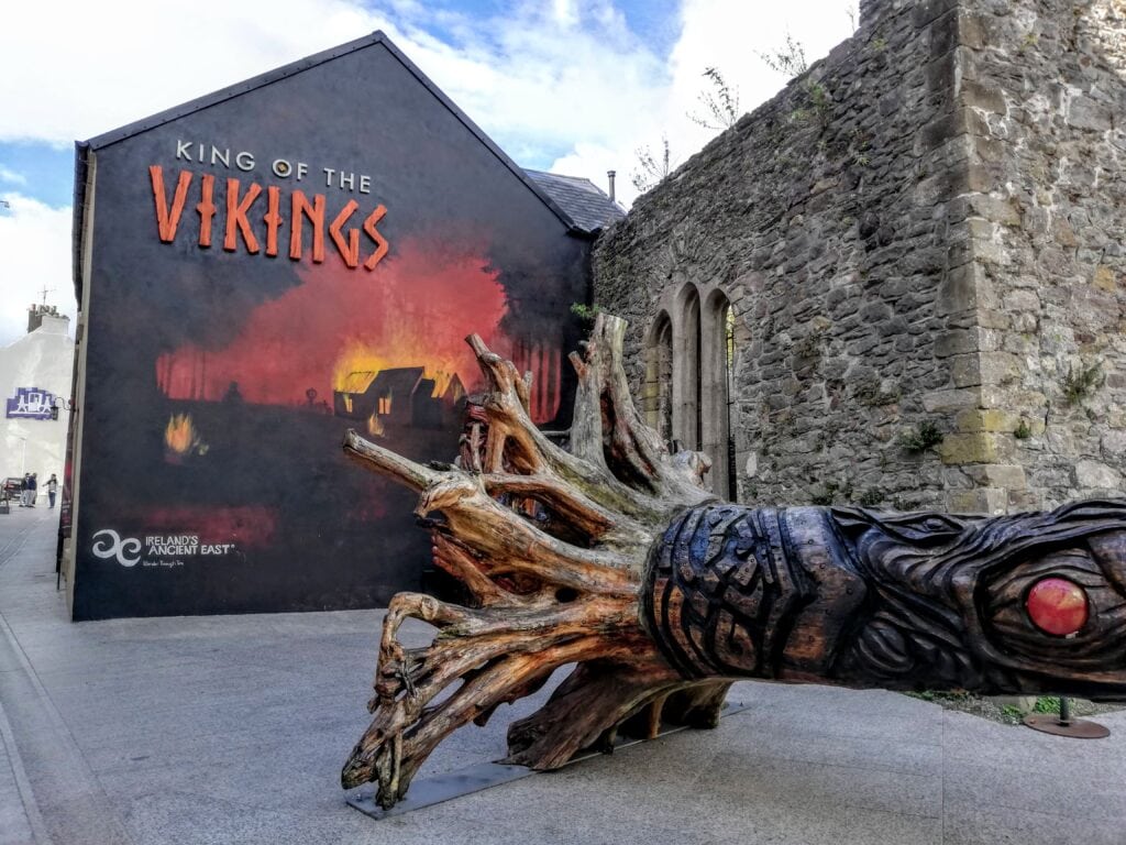 my favourite place on my Irish bucket list exploring the Viking Triangle in Waterford. a stone ruin stands beside an intricately carved tree trunk representing the vikings in Ireland.