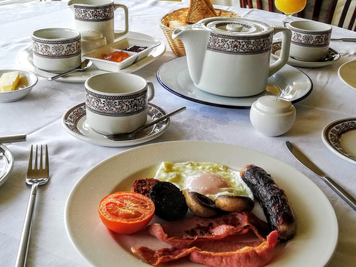 A full Irish breakfast white plates and a tea service with fried egg, black and white pudding, tomatoes, sausages, Irish bacon, mushrooms all served in the best places to eat in Donegal