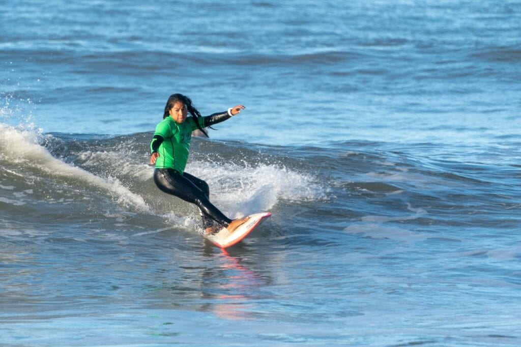 Woman in green wetsuit is concentrating while surfing. Best surfing beaches in the UK
