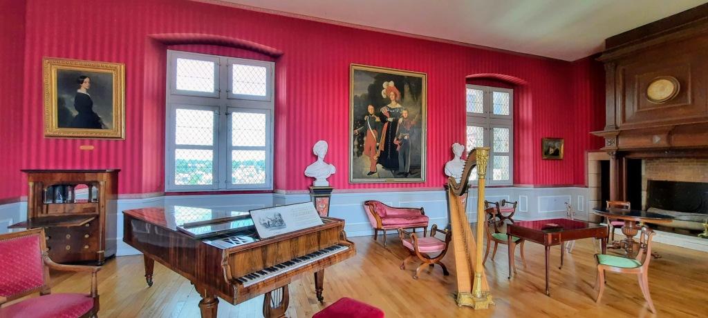 The music room at the Chateau Amboise. Filled with a harp, spinet and a red chaise longue with striped red wallpaper