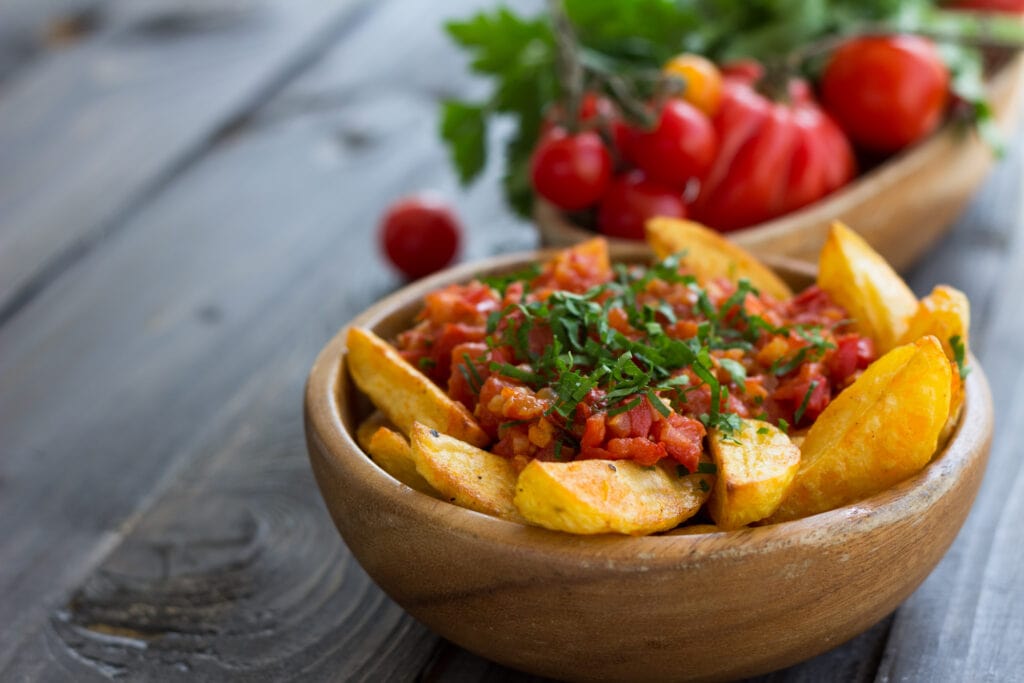 Patatas Bravas, traditional Spanish tapas, baked potatoes with spicy tomato sauce in wooden bowl on wooden table. selective focus