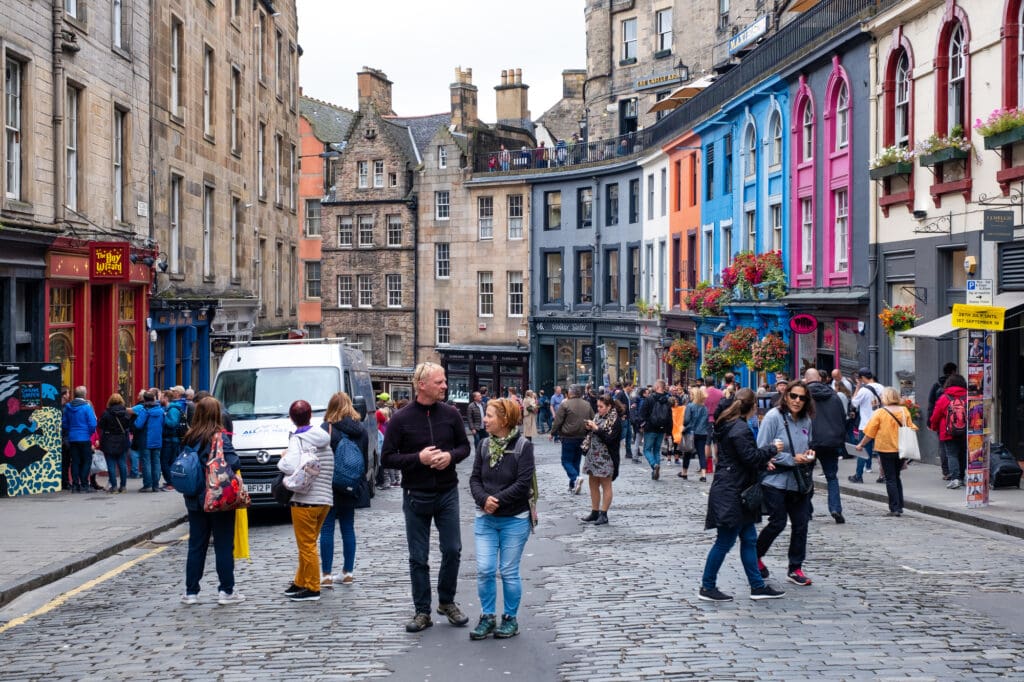 things to do in Edinburgh the Royal Mile with a curved row of colourful houses and loads of folks walking around the independent shops and enjoying the cafe

