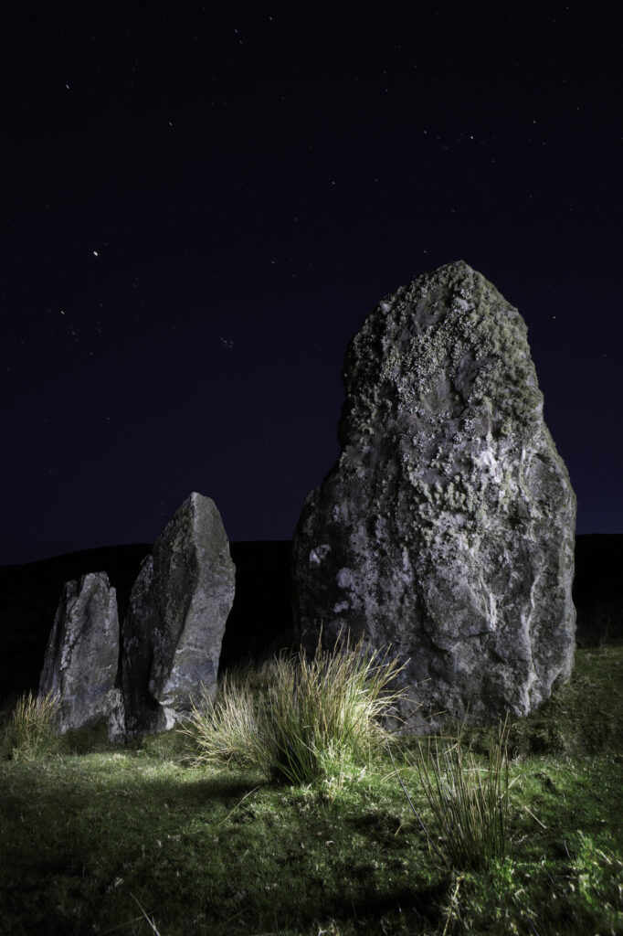 Three standing stones at Cloghan, Dingle peninsula, Kerry Distric Ireland. Megalith of Celtic stone age at night under a clear sky. Mystical menhir monument of prehistoric era and old culture. Landscape lightpainting
