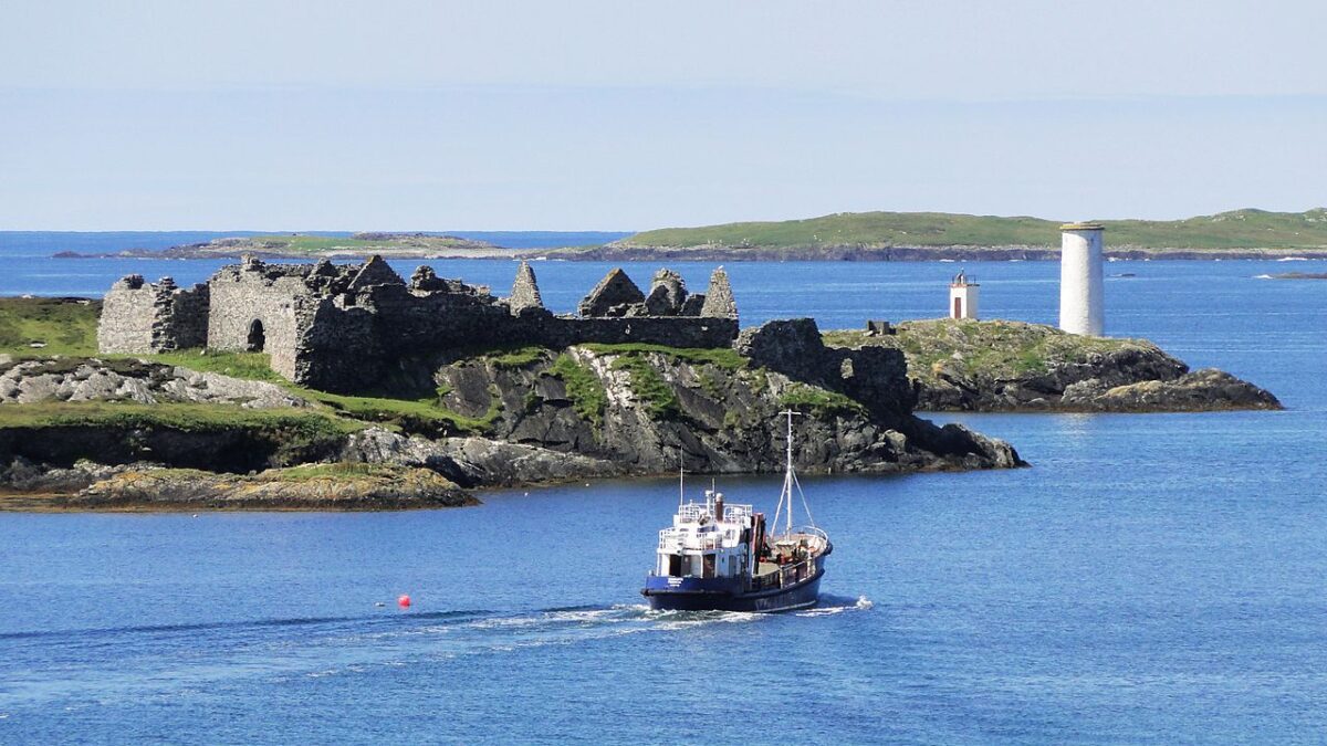 Inishboffin Island off the coast of the WAW with small boats in the sea and a ruin and a lighthouse on the tip of the island