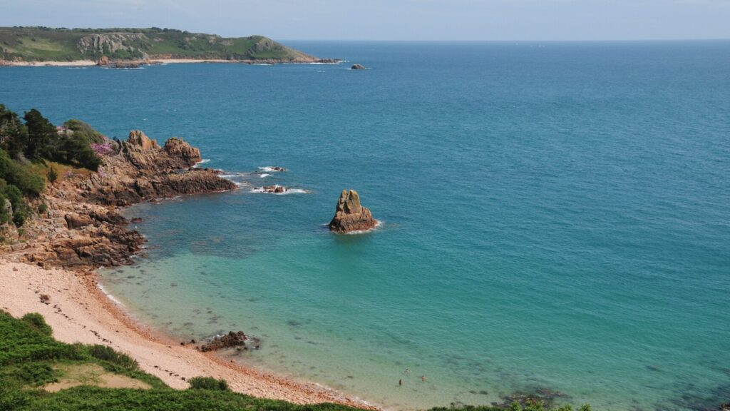 A gorgeous nearly deserted beach with fluffy white clouds and a small island with a ruin on it. The perfect staycation - Jersey Holidays.