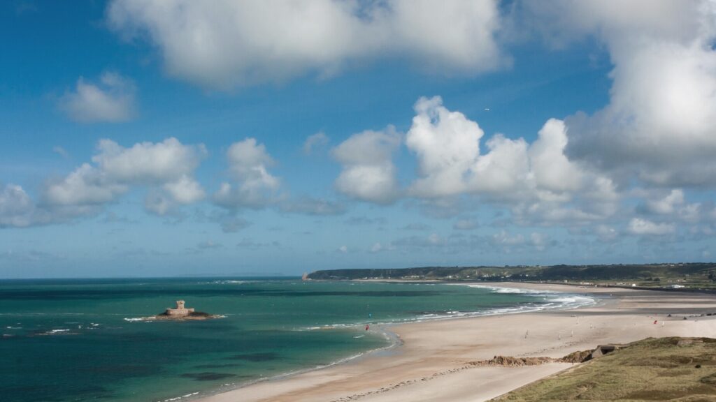 A gorgeous nearly deserted beach with fluffy white clouds and a small island with a ruin on it. The perfect staycation - Jersey Holidays.