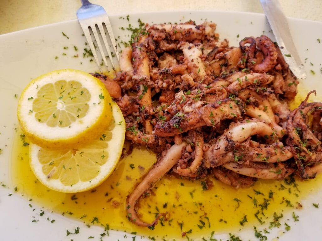 Fried octopus with lemon and spices on white plate with fork and knife in summer street cafe in Marsaxlokk, Malta