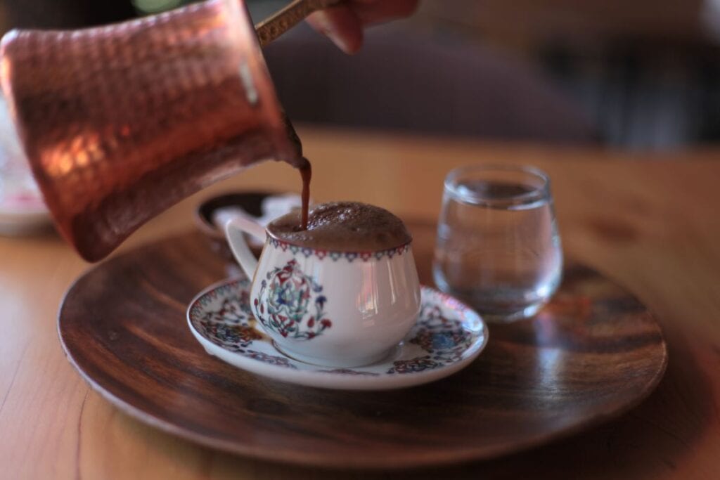 Traditional Turkish coffee, a popular food of Cyprus, is expertly poured into a delicate cup on a rustic wooden table.