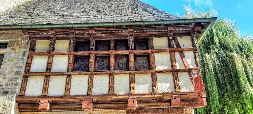 A close up view of a medieval building in Dinan France with carved figures decorating the half-timbered top of the building. The carvings depict saints, animals and Brittany's royals