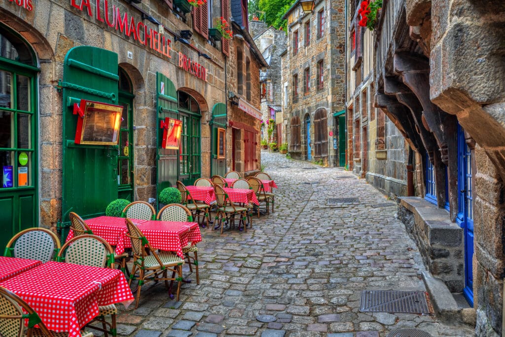 Dinan, France - 10 July 2017: Typical narrow cobbled street with outdoor cafes in the historical Old town of Dinan. Dinan is a popular tourist destination in Brittany, France.