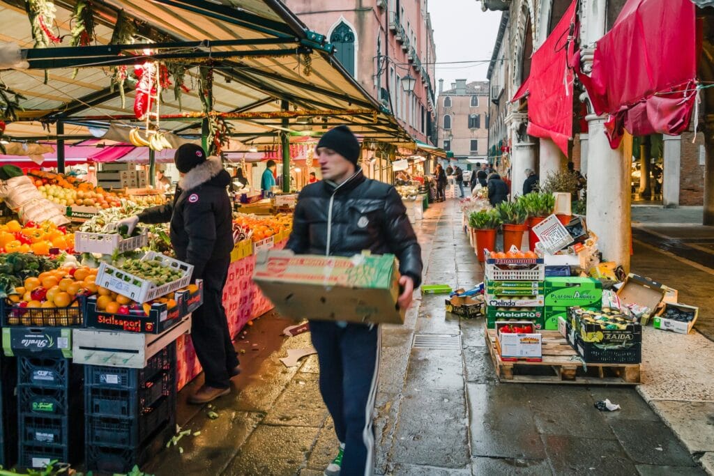VENICE, ITALY - December 24, 2012. A market trader carries crates of vegetables to a traditional European open market stall at Mercato di Rialto, Venice, Italy