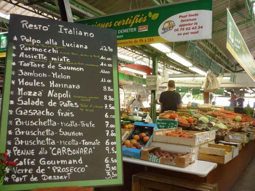 A famous food market in Europe in Paris with a fruit and vegetable stall and a sign advertising all kinds of french foods to purchase. 