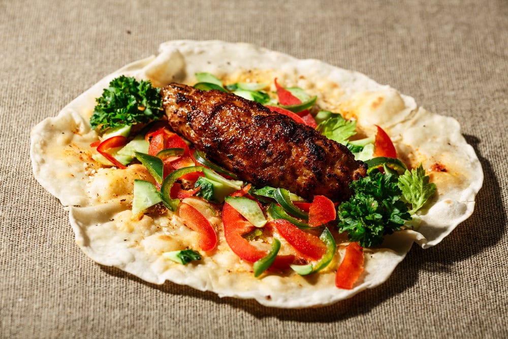 Shish kofte (kofta kebab) with vegetables and herbs on naan or lavash or pita flatbread