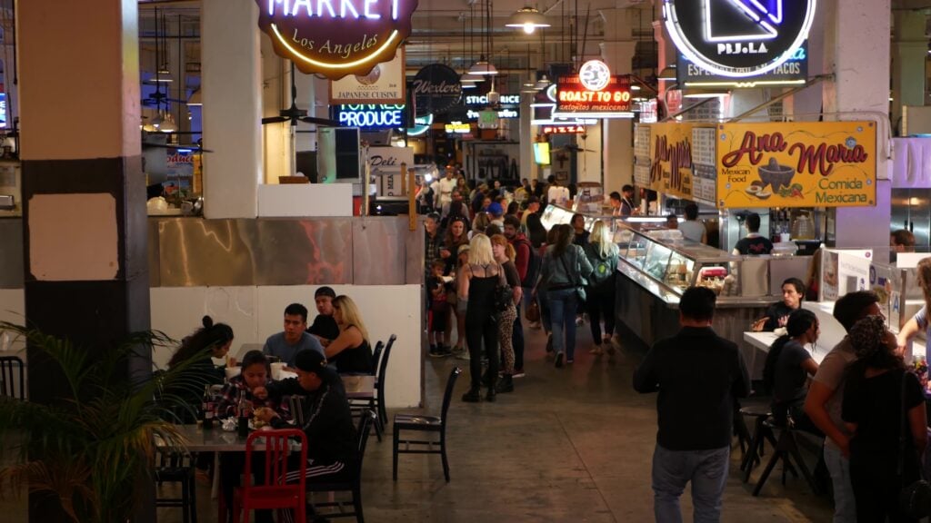 LOS ANGELES, CALIFORNIA, USA - 27 OCT 2019: Grand central market street lunch shops with diversity of glowing retro neon signs. Multiracial people on foodcourt. Citizens dining with fast food in LA.