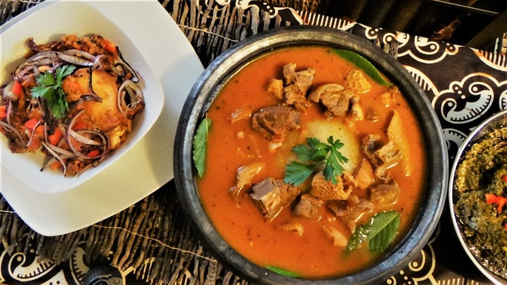 Fufu from West African nations the bowl in the middle is full of mutton stew and the bowl on the left is a ball of pale cream coloured fufu served with crispy red onions