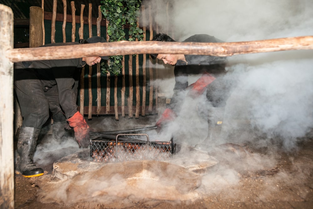 Rotorua New Zealand - April 2014; Smoke and dust fly as food is being prepared for a traditional maori feast or Hangi, by steaming through heat from underground thermal activity or heated stones in base of pit.