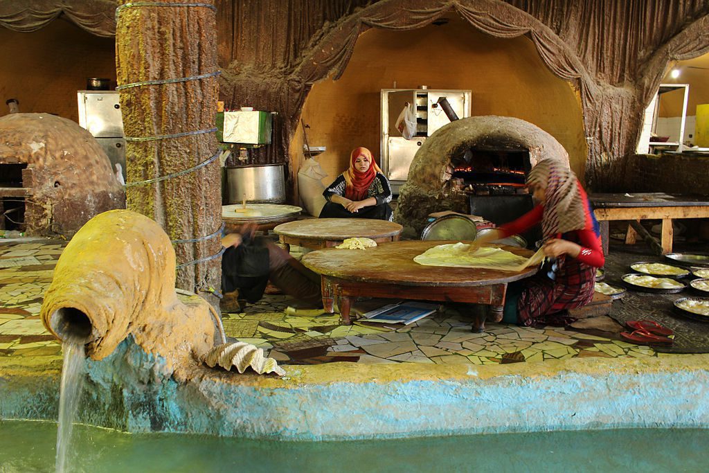 two women sit in a house with large clay ovens making the fattah bread